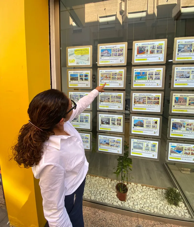 Elva Zamudio señalando fichas de viviendas en el escaparate de Wereal Grupo Inmobiliario